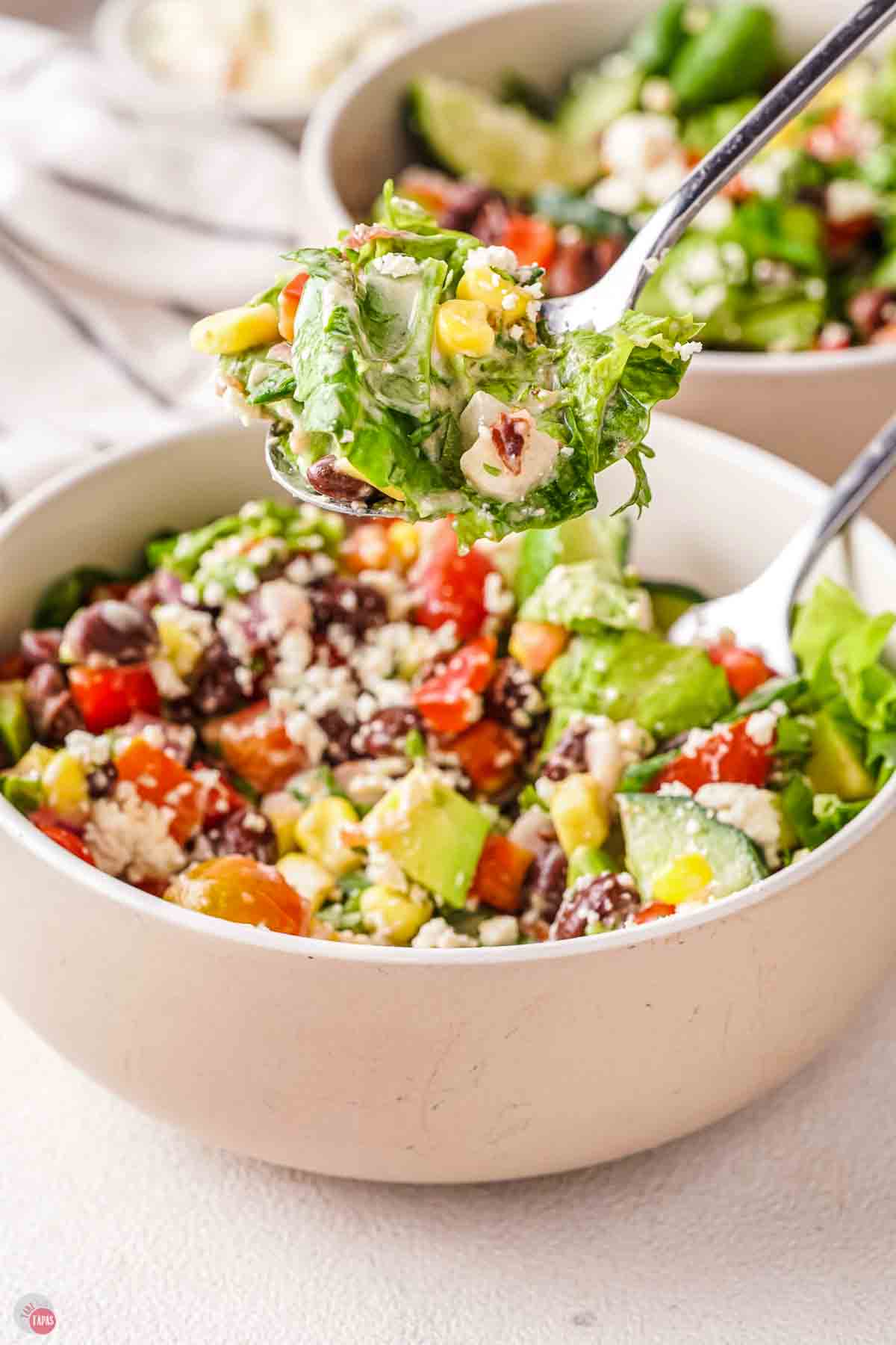 white bowl of salad with tongs grabbing some out of it