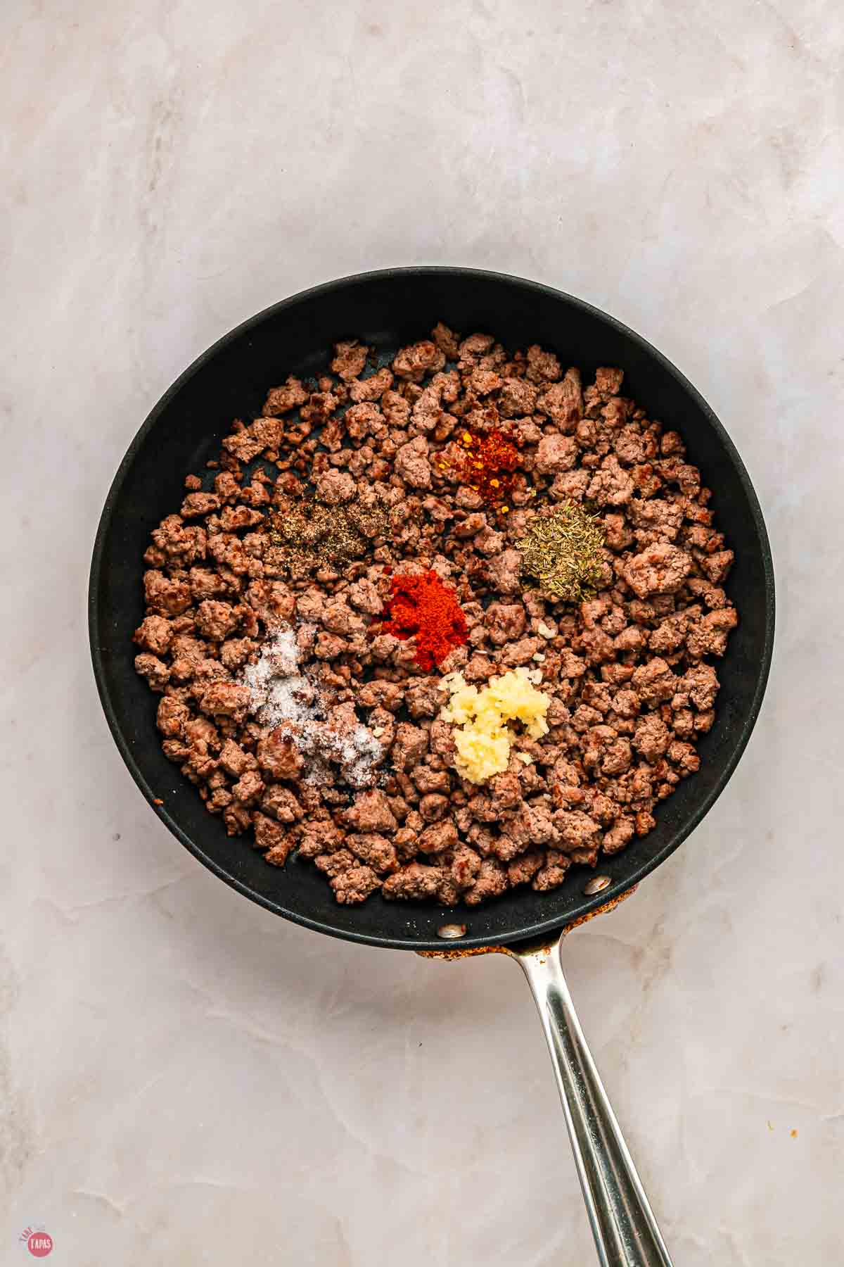 ground beef in a skillet with some spices sprinkled on top