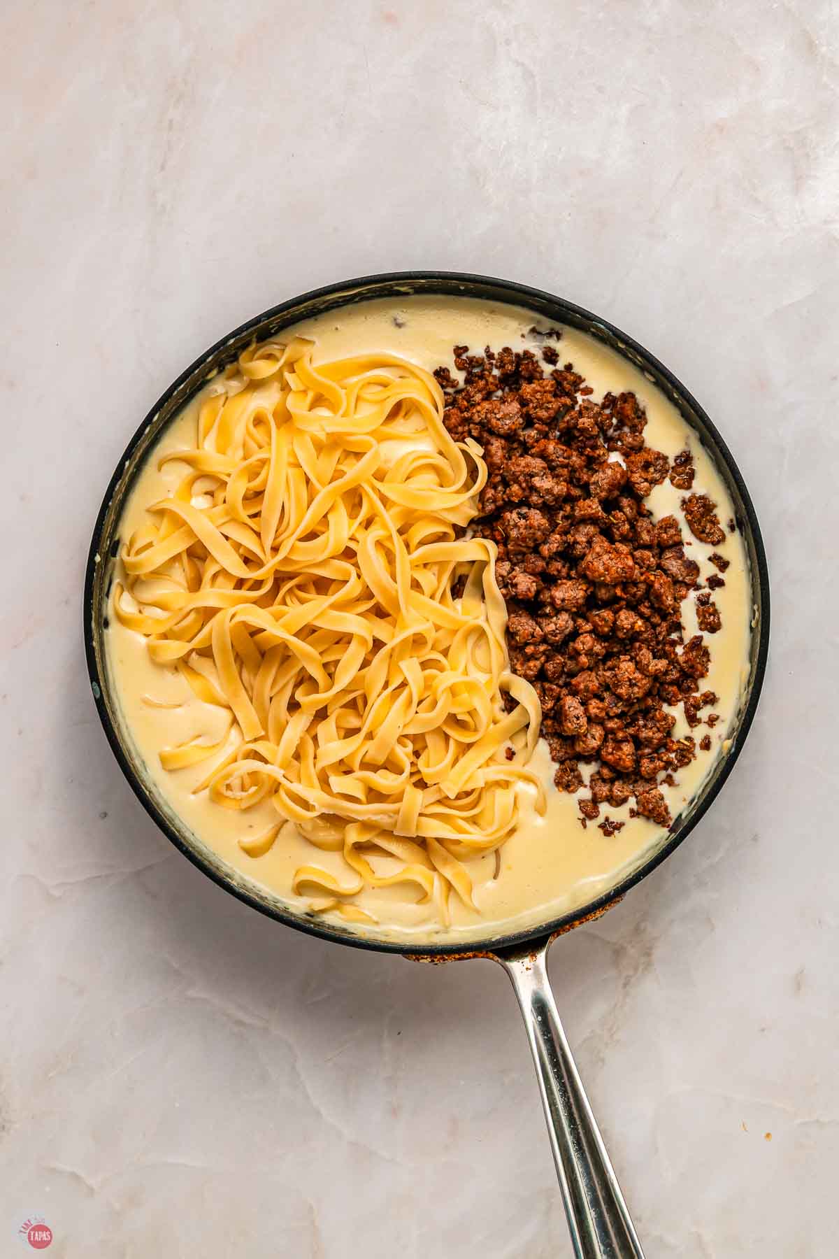 skillet with cream sauce and a two piles or pasta and cooked ground beef on top