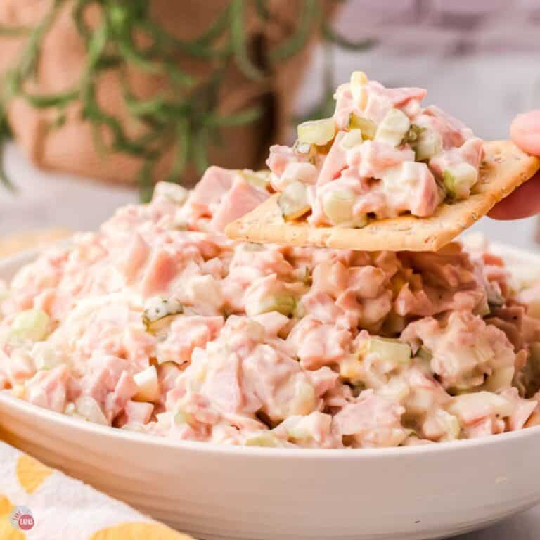 bowl of ham salad with a hand holding a cracker with some on it