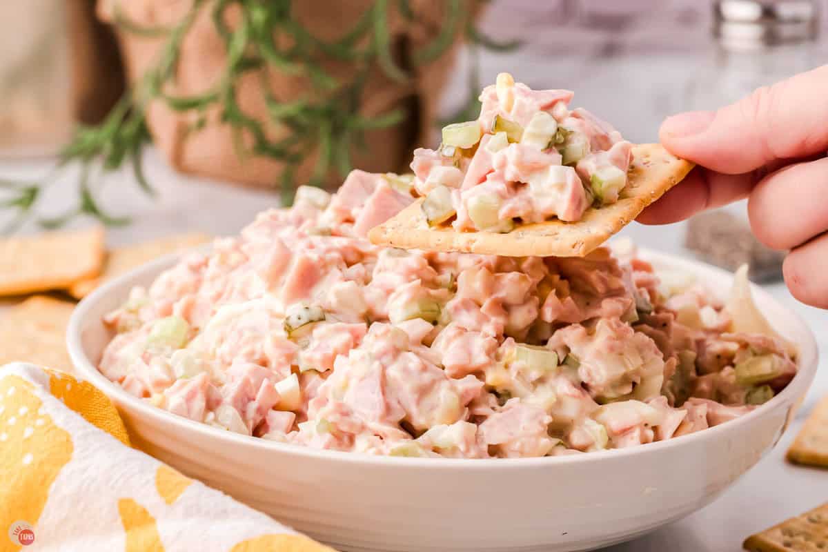 bowl of ham salad with a hand holding a cracker with some on it