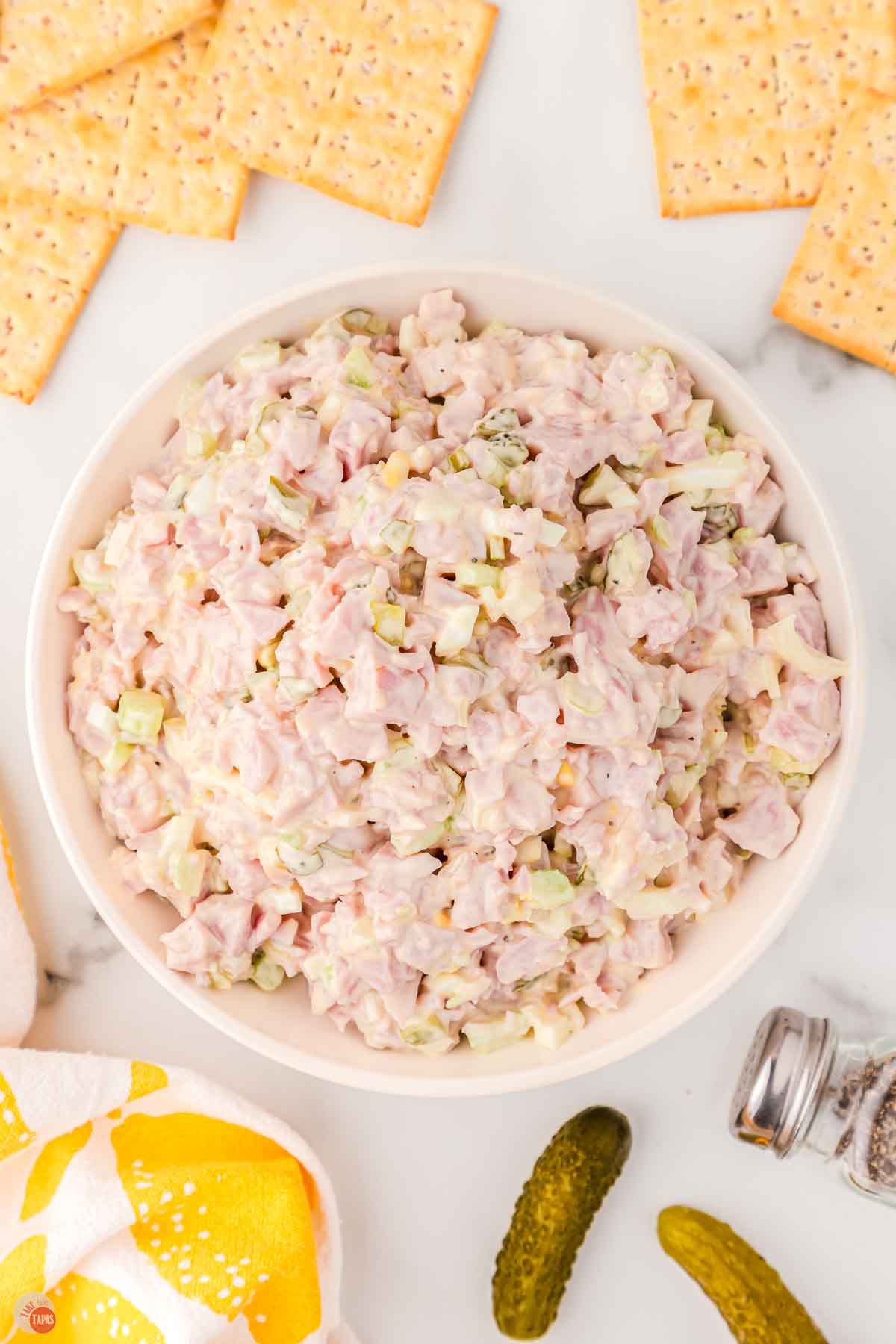 white bowl full of ham salad with some crackers on the counter around it