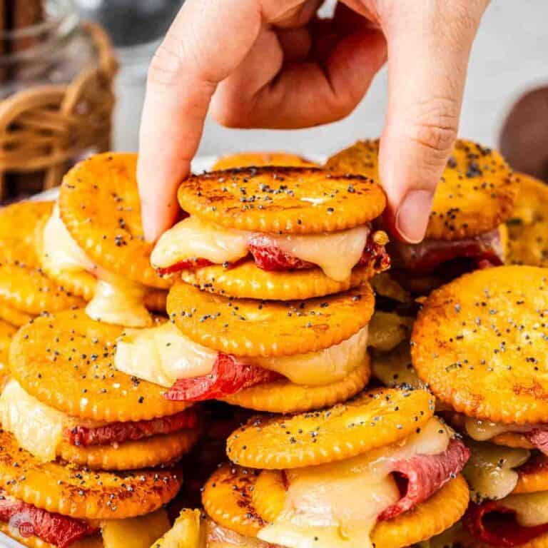 Hand grabbing a Ritz sandwich off a plate with stacks of them