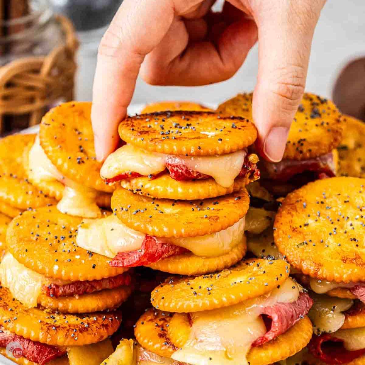 Hand grabbing a Ritz sandwich off a plate with stacks of them