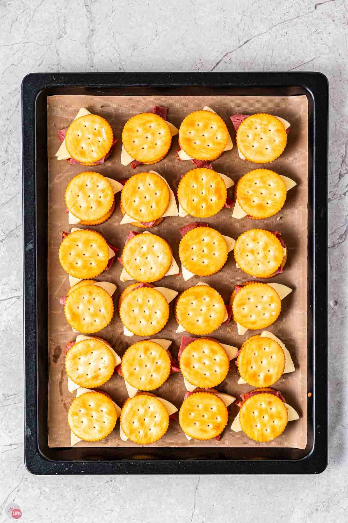 cracker stacks filled with roast beef and provolone on a baking sheet with parchment paper
