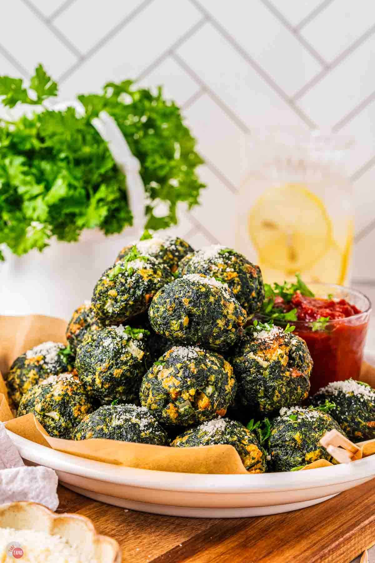 spinach balls on a yellow plate with a bowl of red sauce