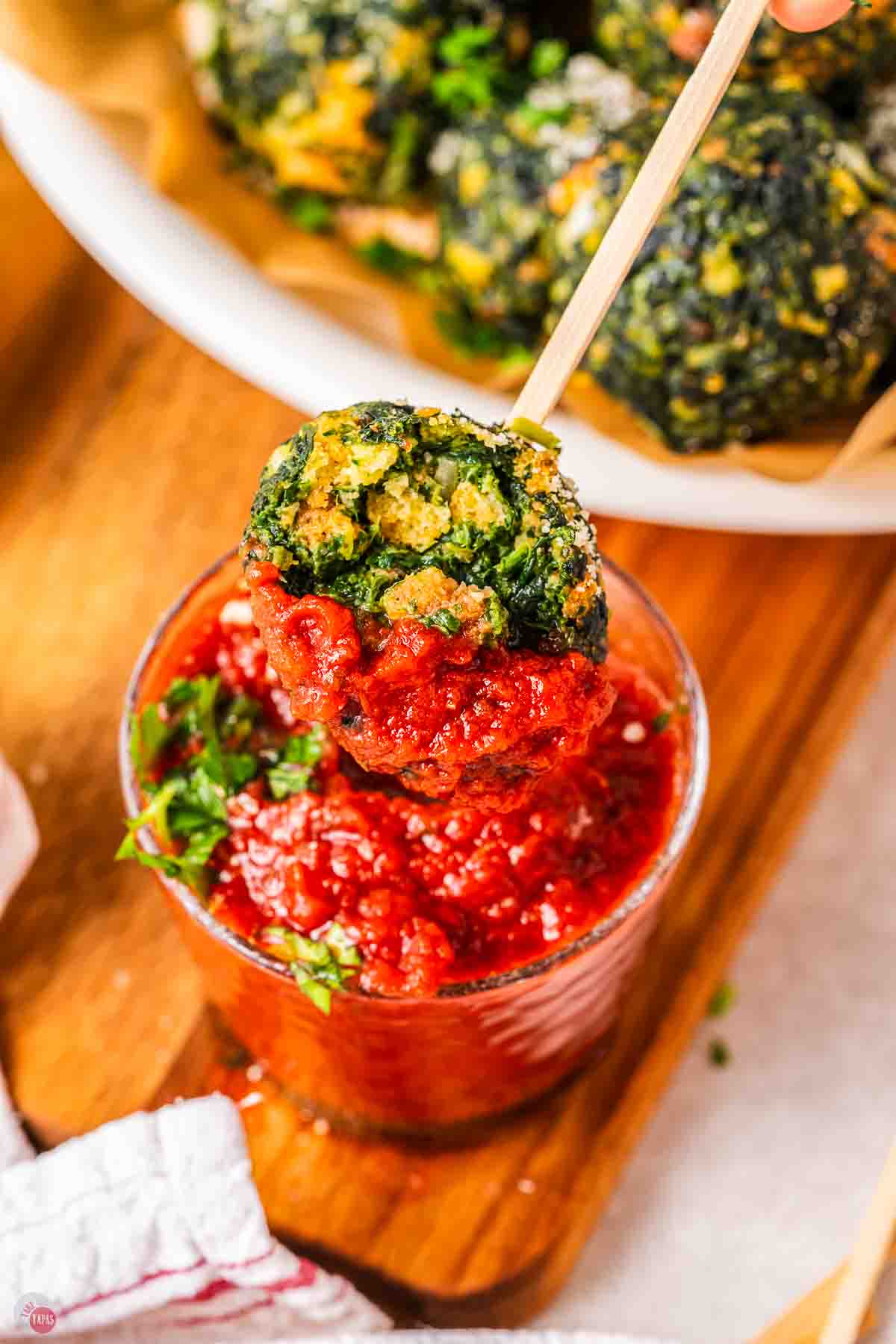 toothpick with spinach ball on it with a bite taken out of it dipped in red sauce