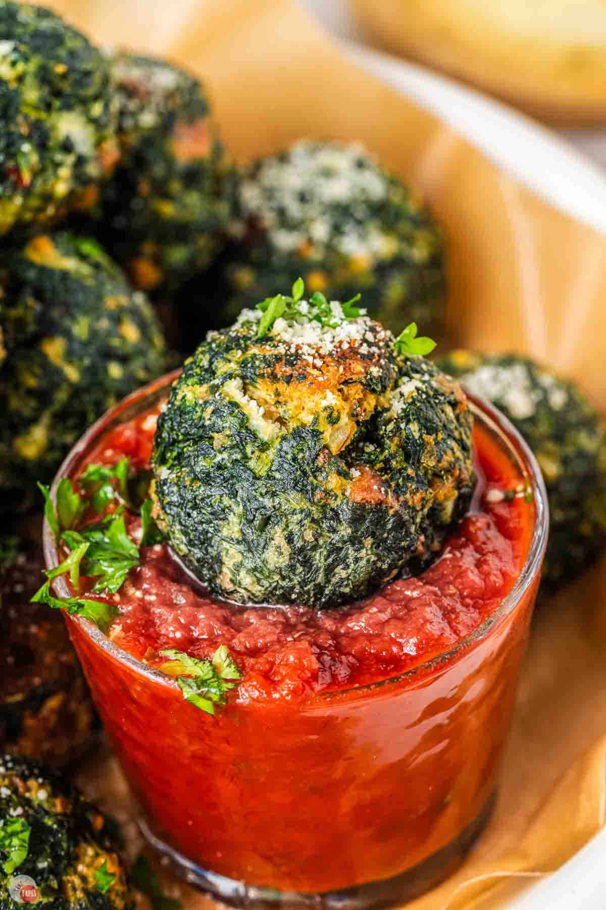close up of spinach ball sitting in a small clear cup filled with red sauce