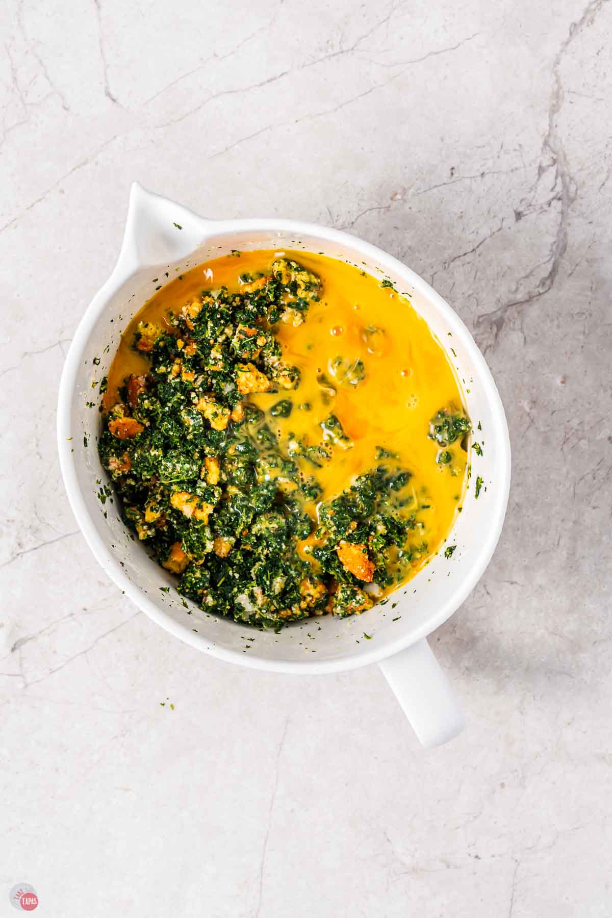 white mixing bowl of spinach mix with beaten eggs
