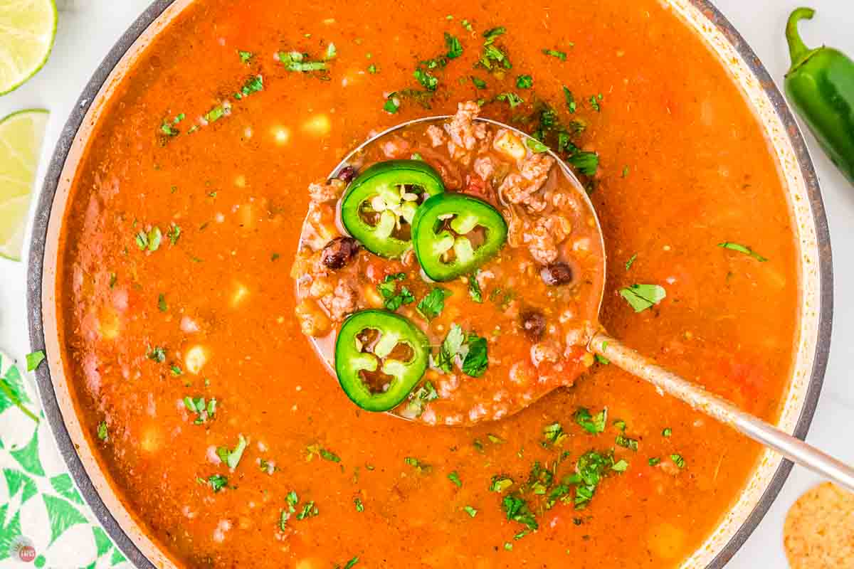 soup with a ladle and sliced jalapeno peppers on it