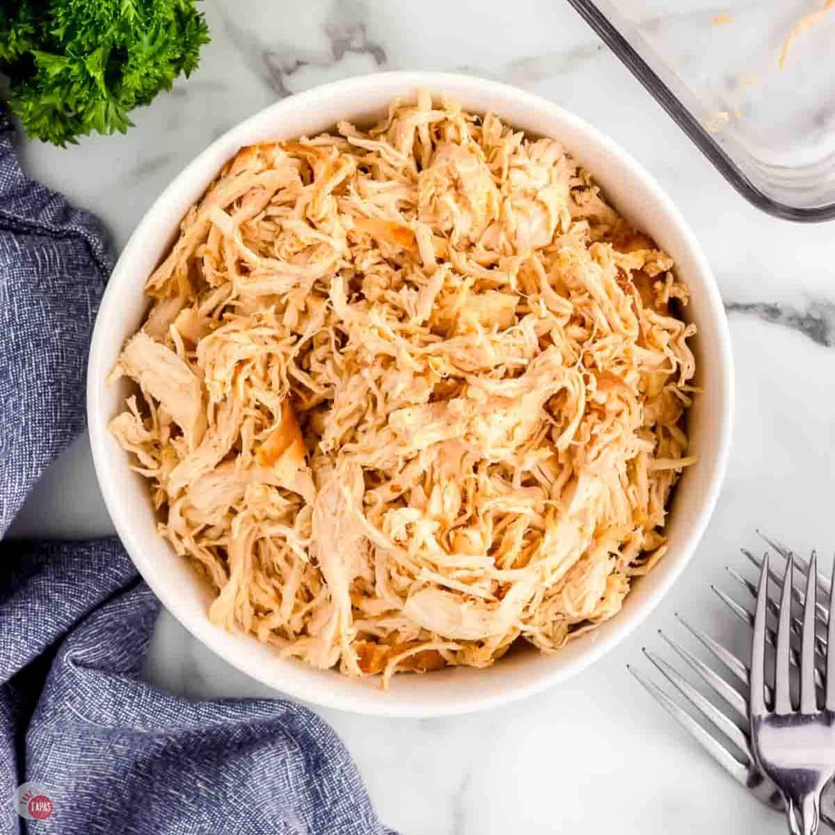 white bowl with shredded chicken and two forks