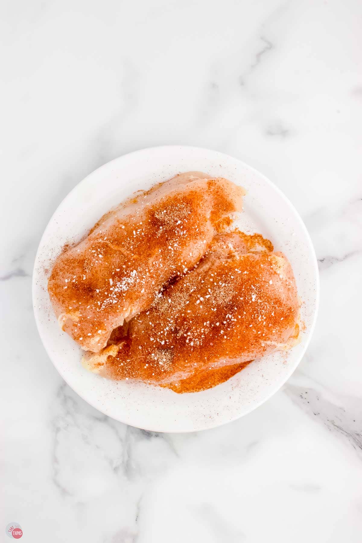 two chicken breasts on a white plate covered in seasoning