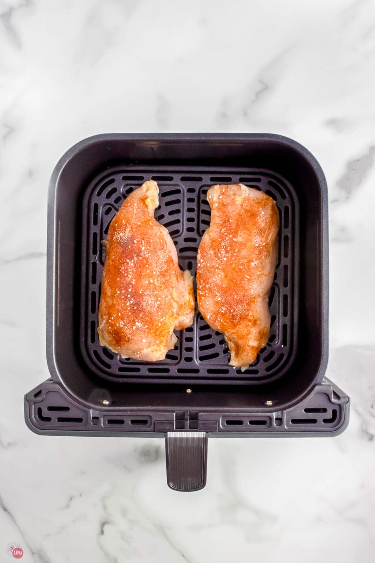 two uncooked chicken breasts in an air fryer basket