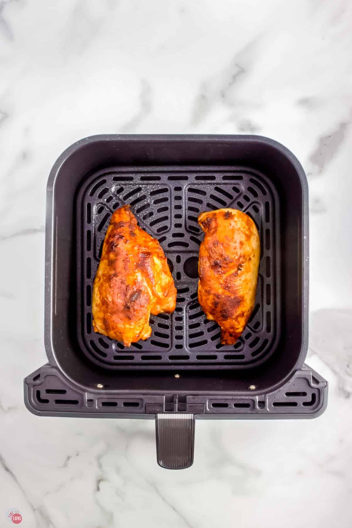 two pieces of cooked chicken in an air fryer basket
