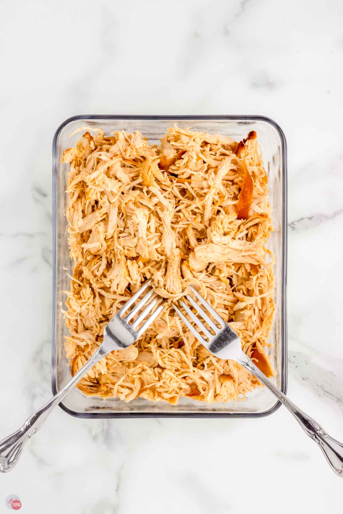 clear baking dish full of shredded white meat chicken with two forks