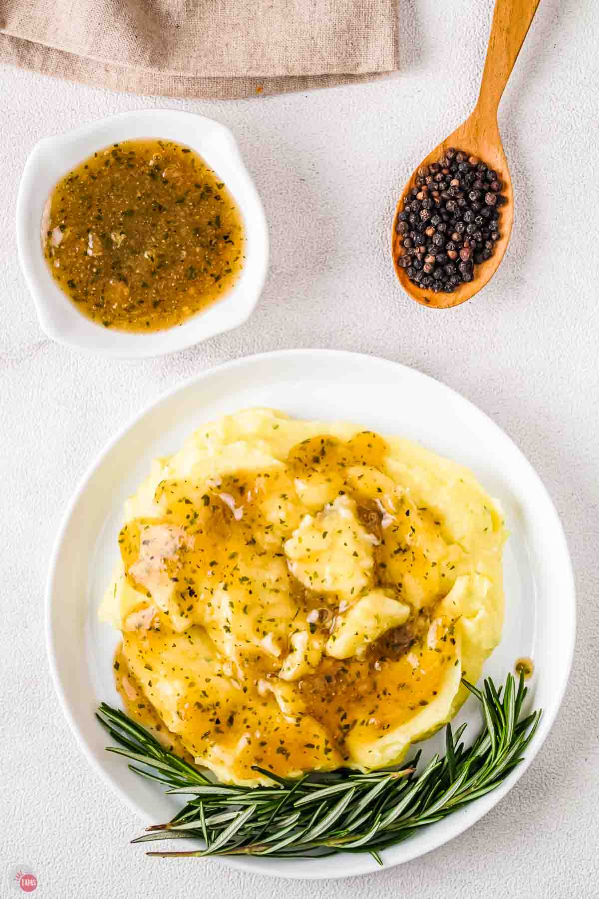 plate of mashed potatoes with au jus gravy on top and a sprig of rosemary