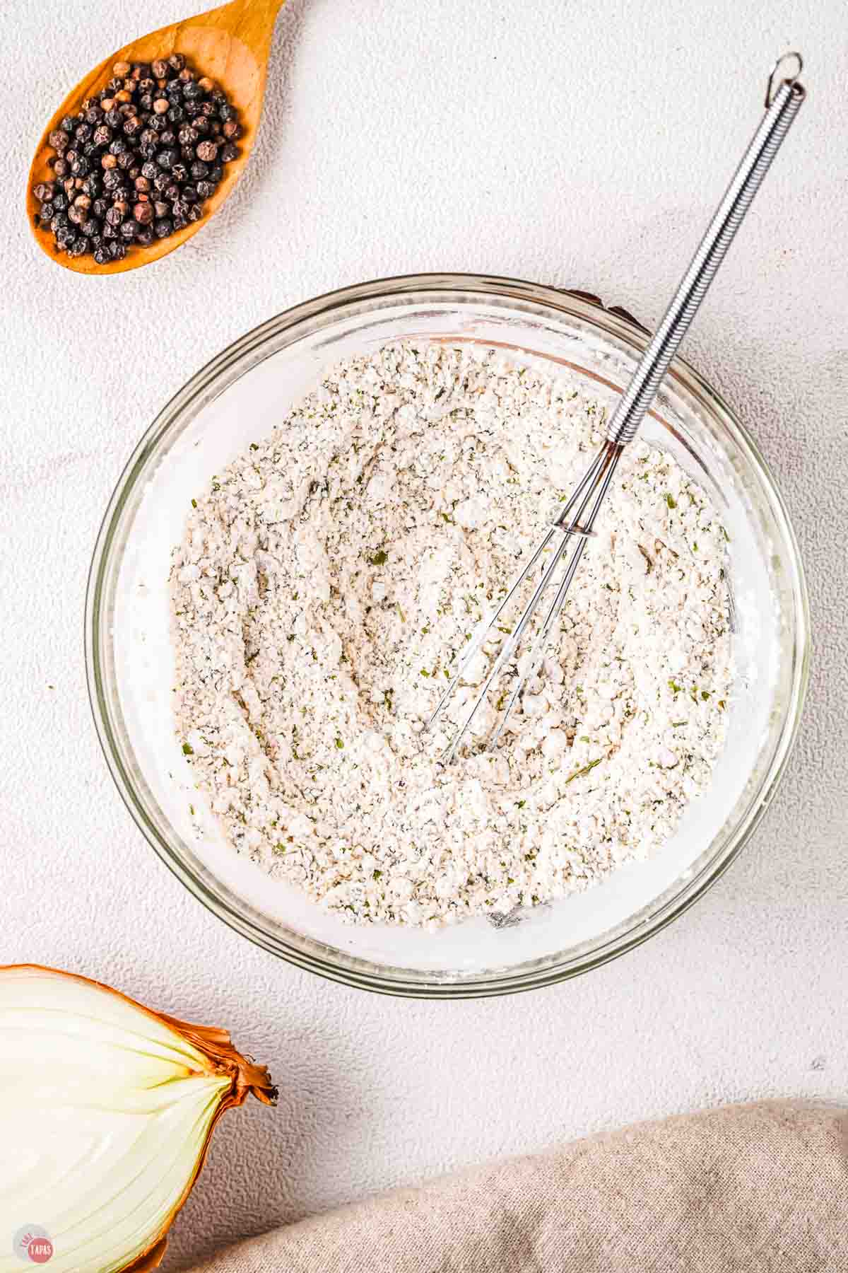 clear bowl with white powder mix being stirred by a whisk
