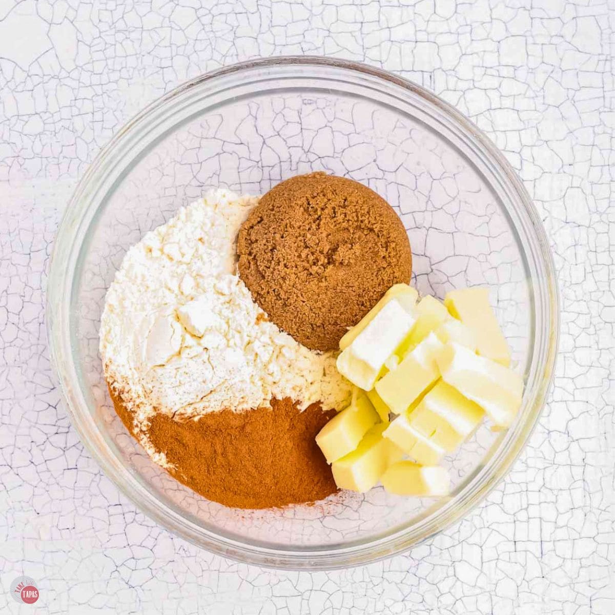 clear bowl with flour, sugar, cinnamon, and cubed butter