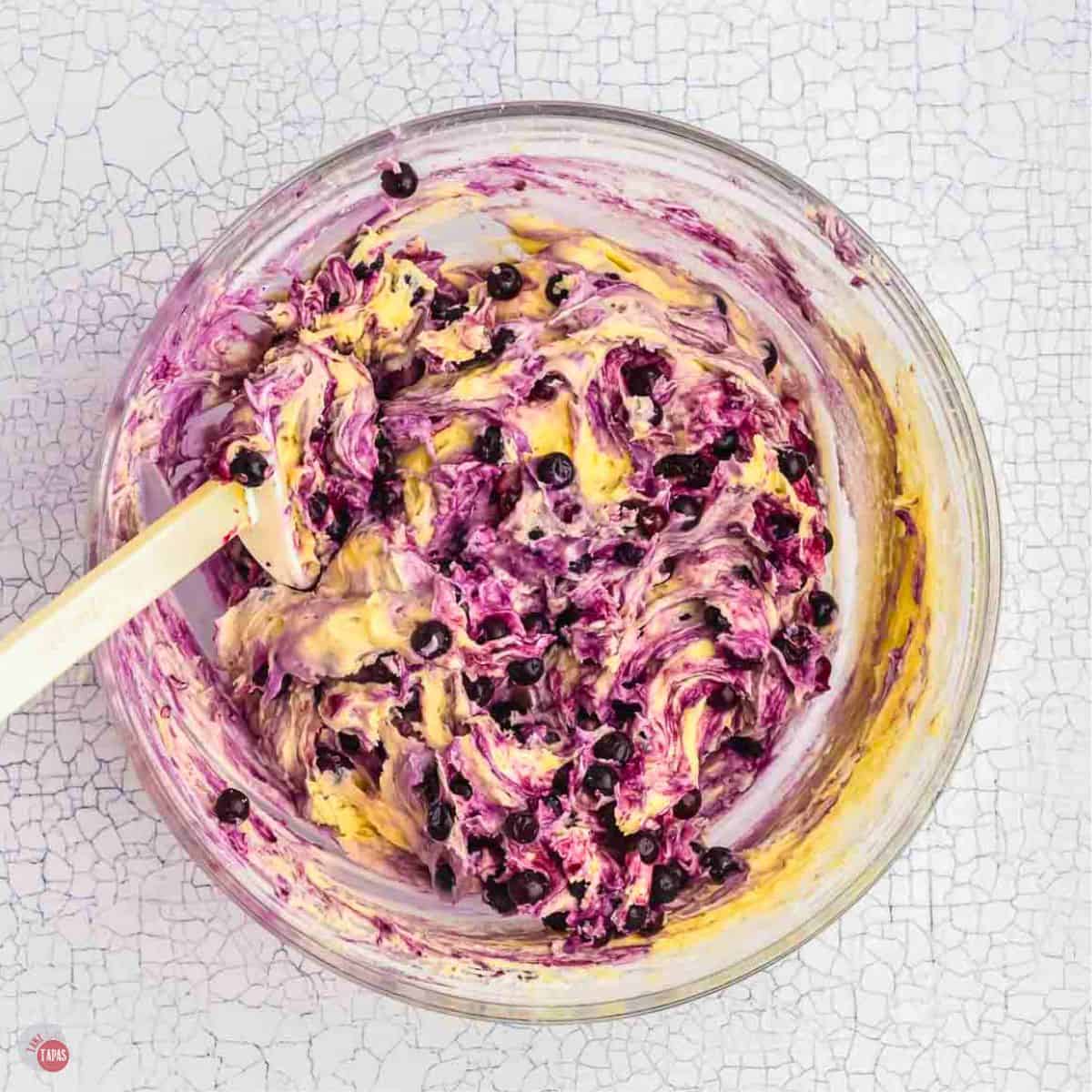 blueberries being mixed in a clear bowl with a white spatula