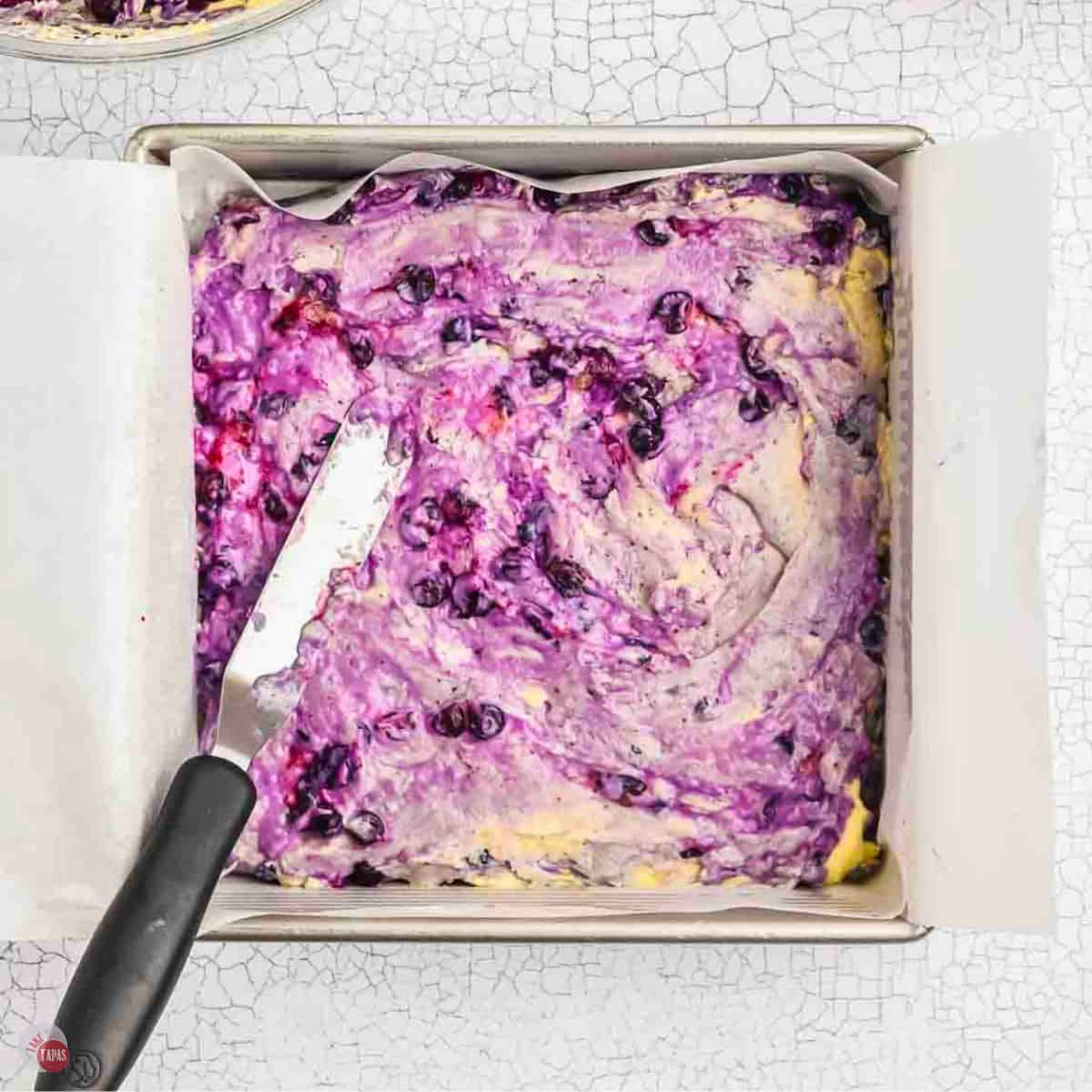 batter being spread into a square baking pan with an offset spatula