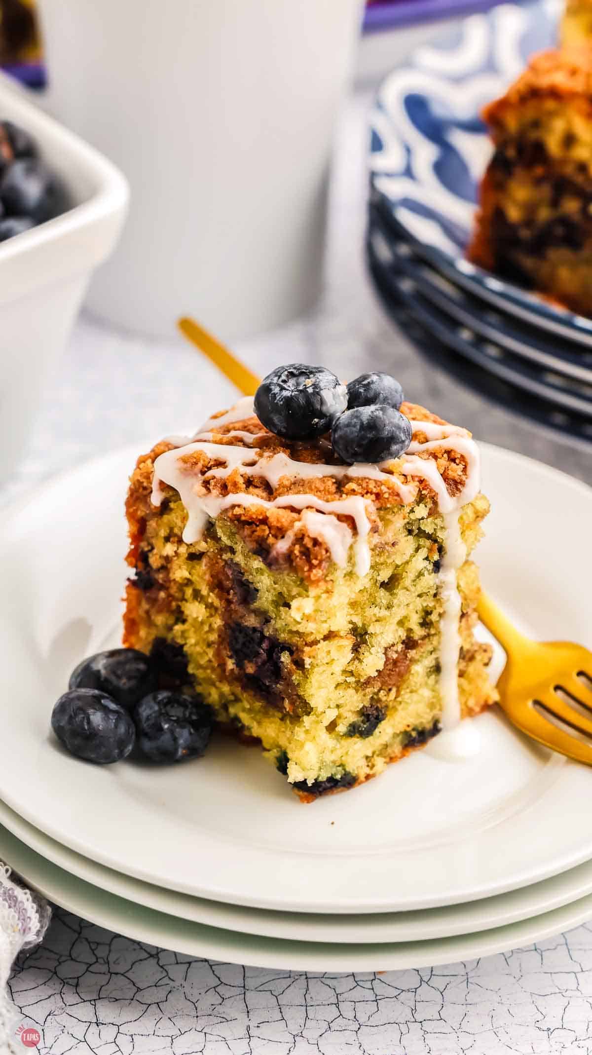 slice of blueberry coffee cake on a white plate with a gold fork