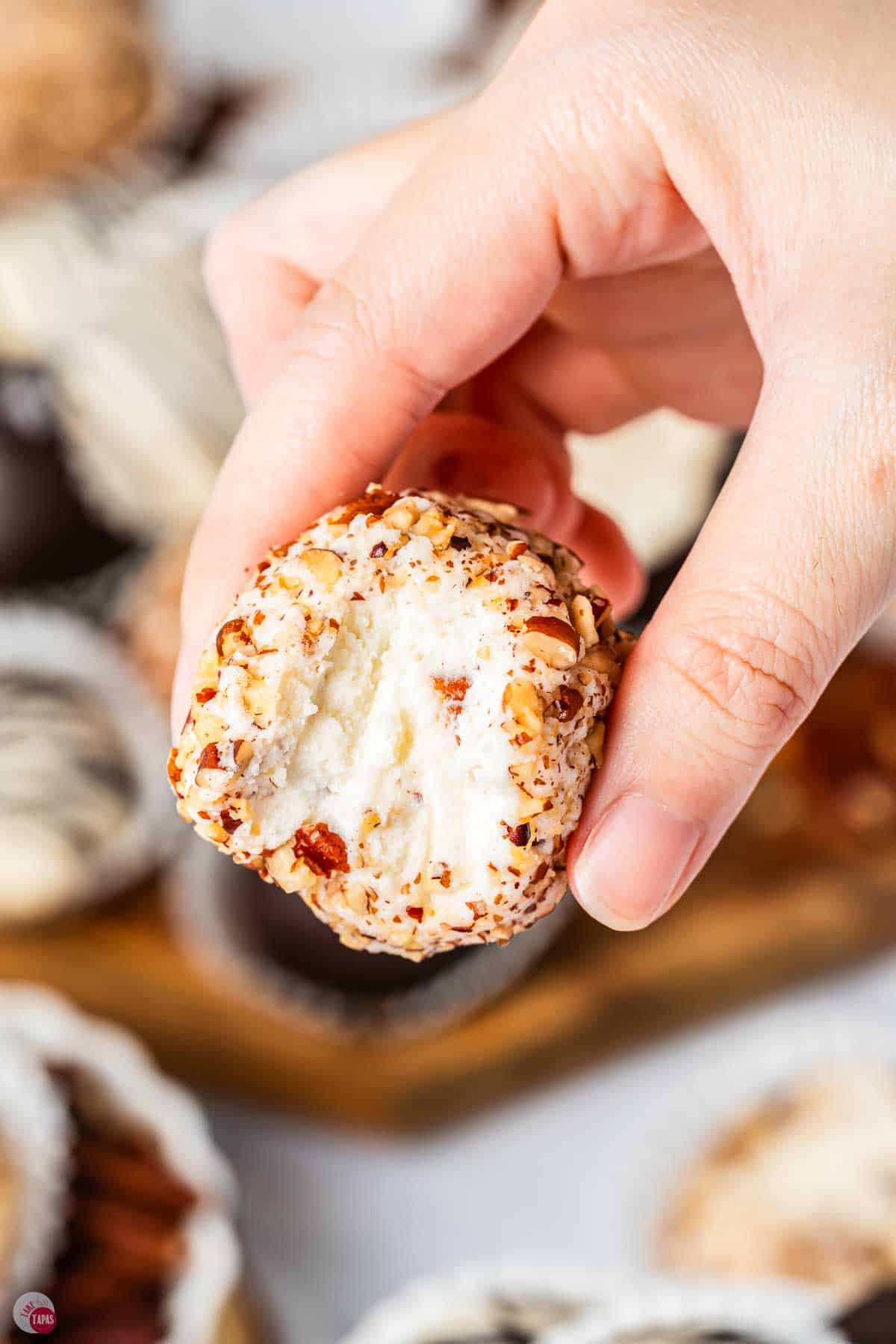 hand holding a bourbon ball coated in chopped pecans