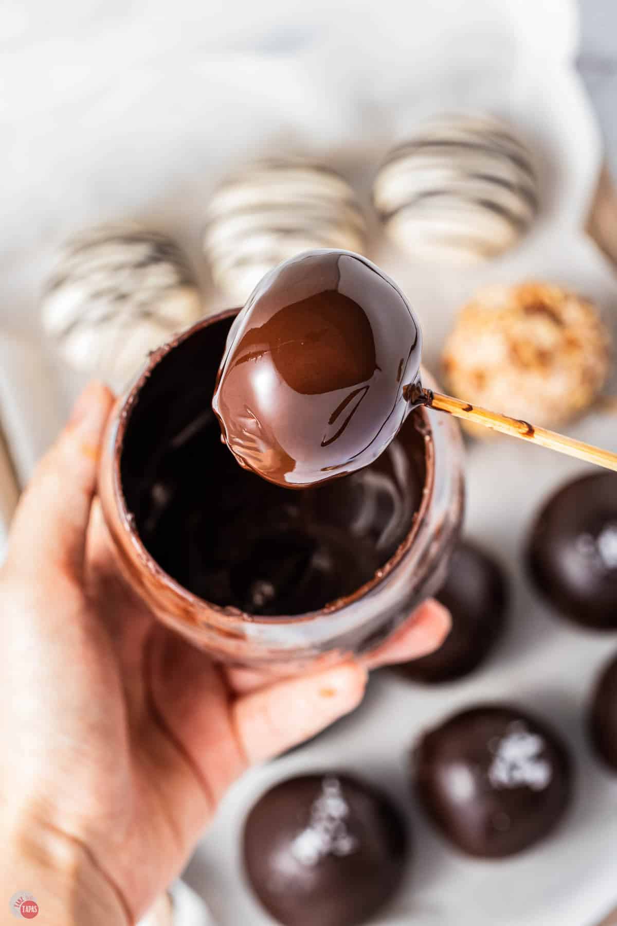 hand with ball on a toothpick being dipped in melted chocolate