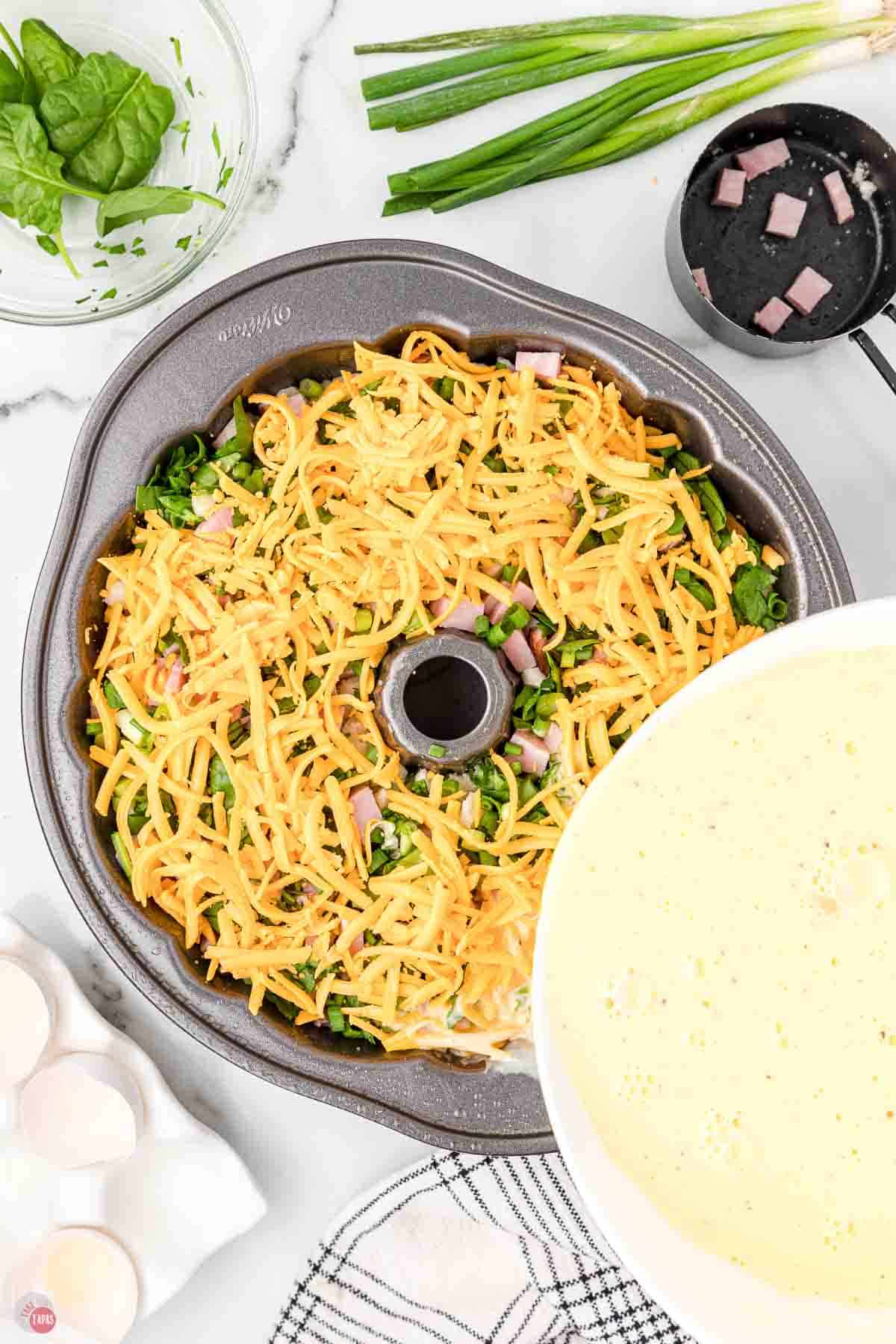 bundt pan with shredded cheese and whisked eggs being poured into it