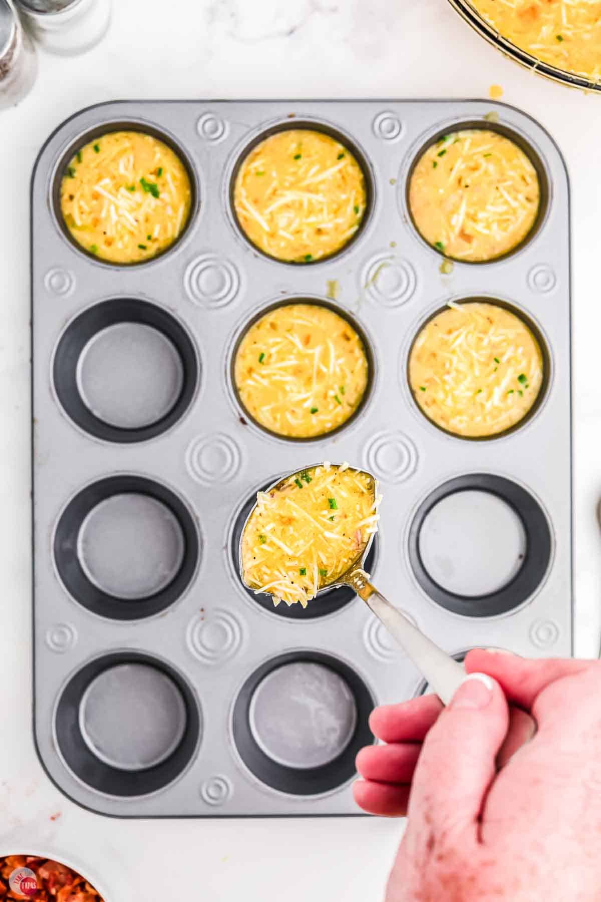 muffin pan with hand spooning in an egg mixture