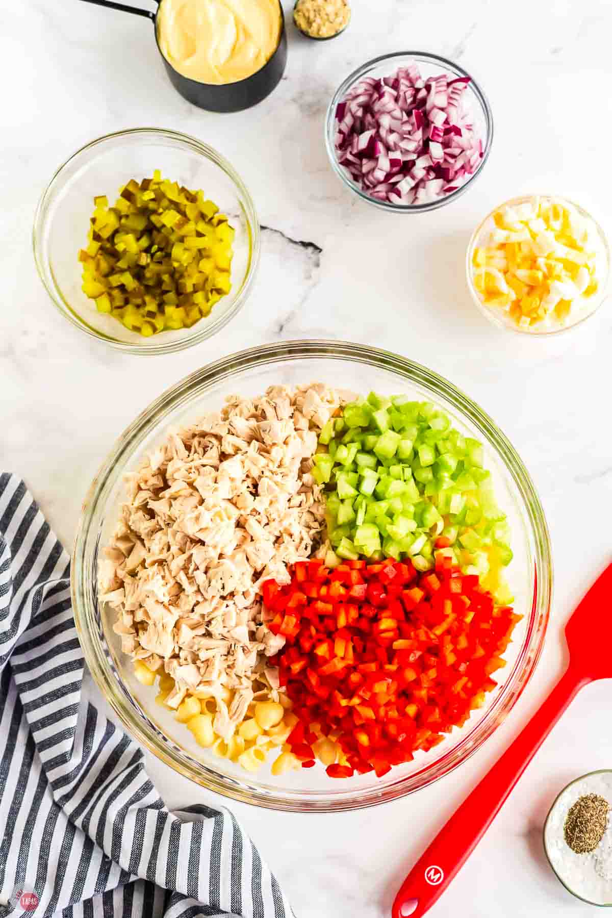 large, clear mixing bowl with cooked pasta, chicken, and diced vegetables