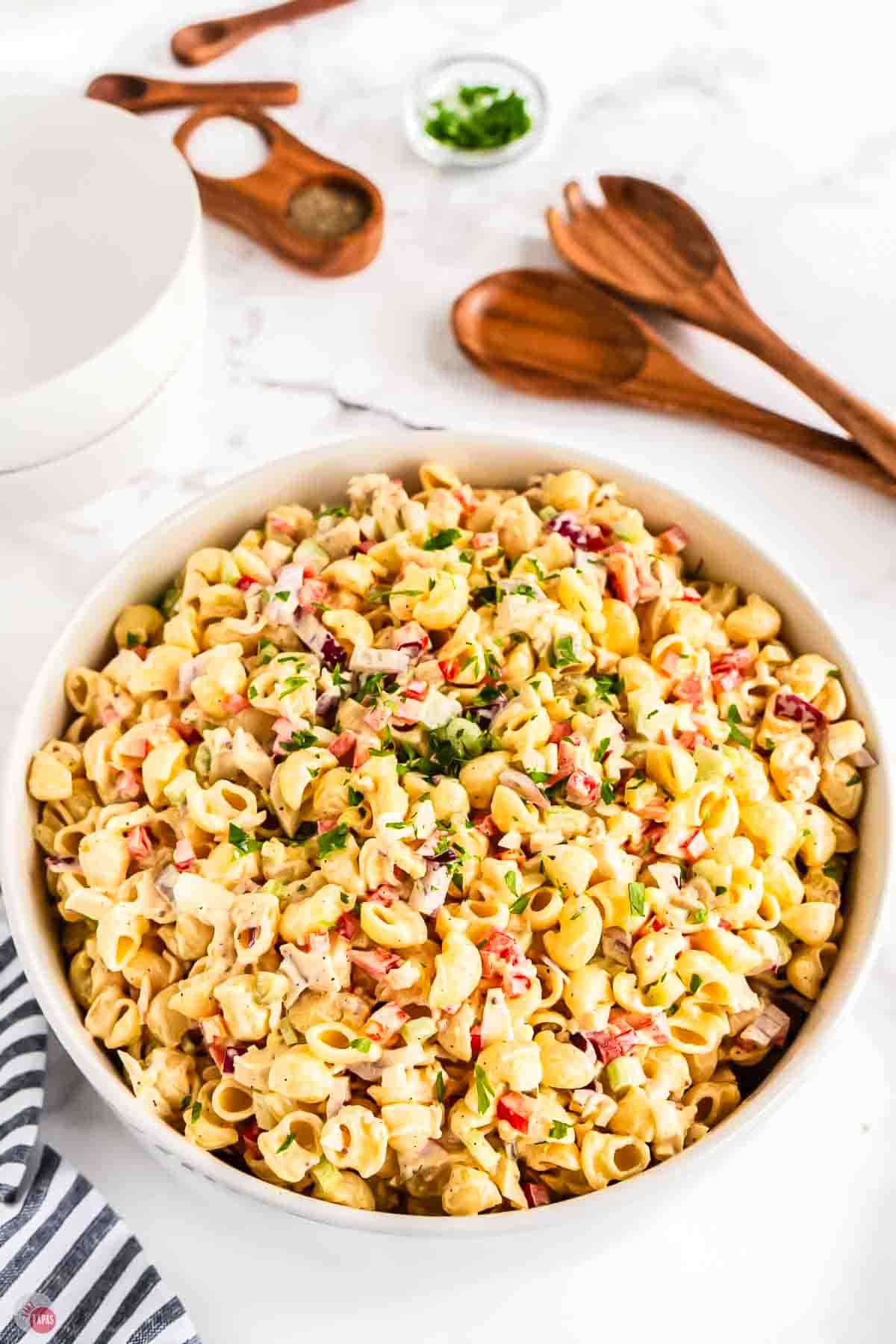 large white bowl of chicken macaroni salad with wood spoons