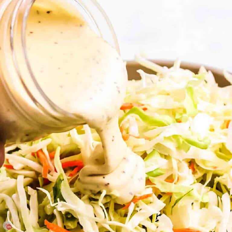 jar of coleslaw dressing being poured over a bowl of shredded cabbage