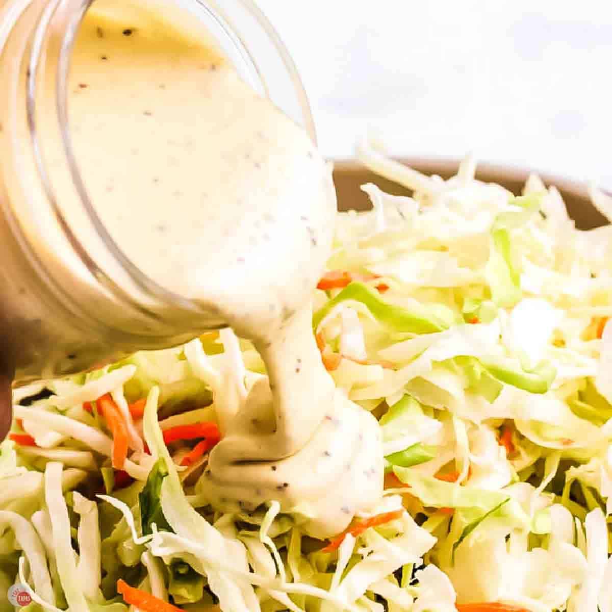 jar of coleslaw dressing being poured over a bowl of shredded cabbage