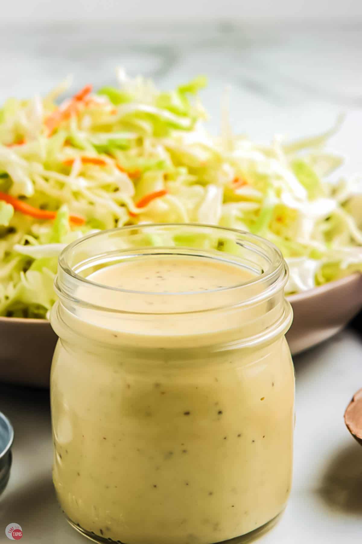 close up of jar of homemade dressing with shredded cabbage in a bowl