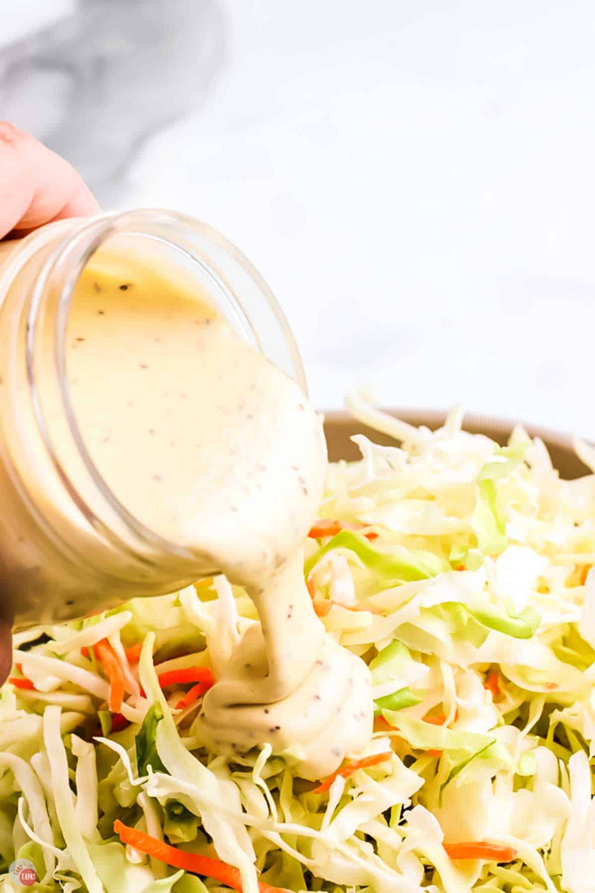 close up of jar pouring dressing on to a cabbage slaw mixture
