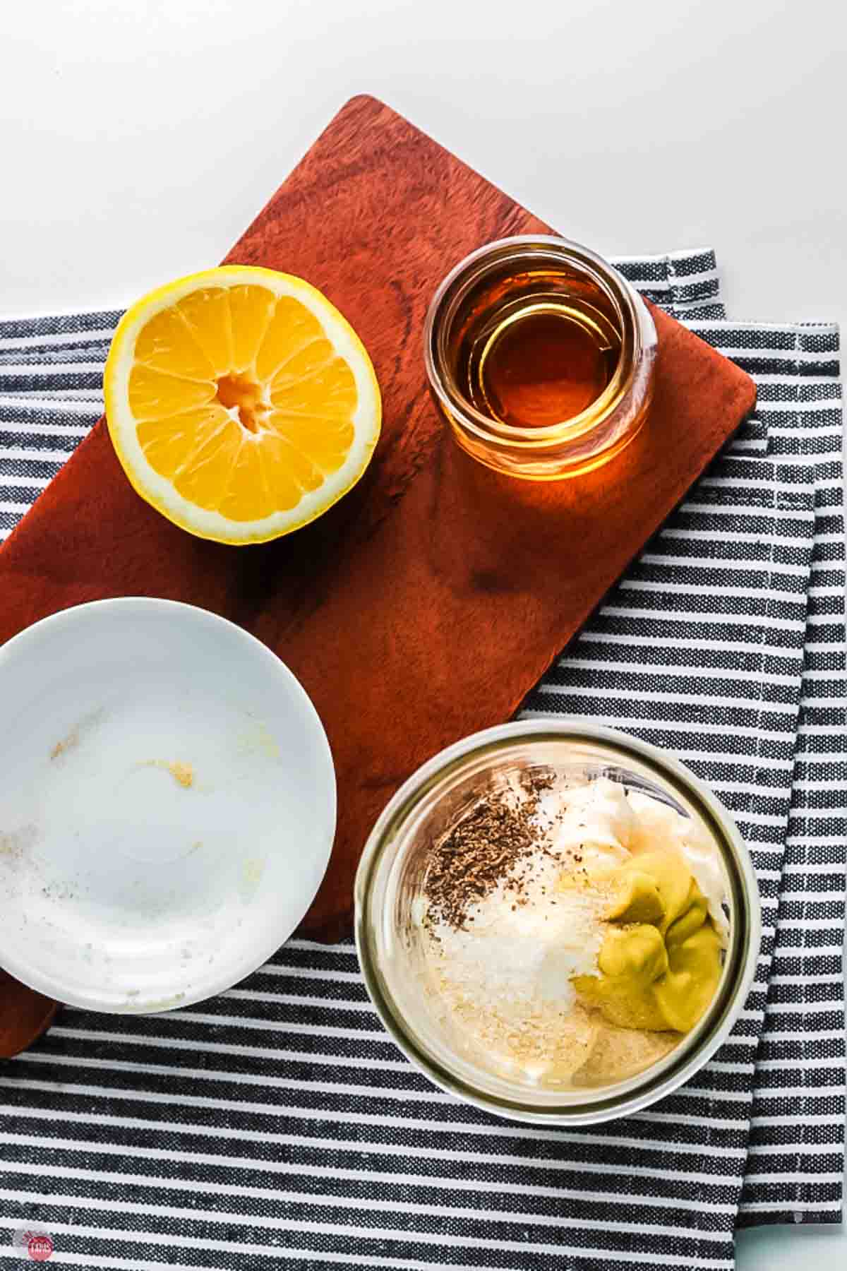 clear jar with dressing ingredients in it next to a sliced lemon and jar of vinegar