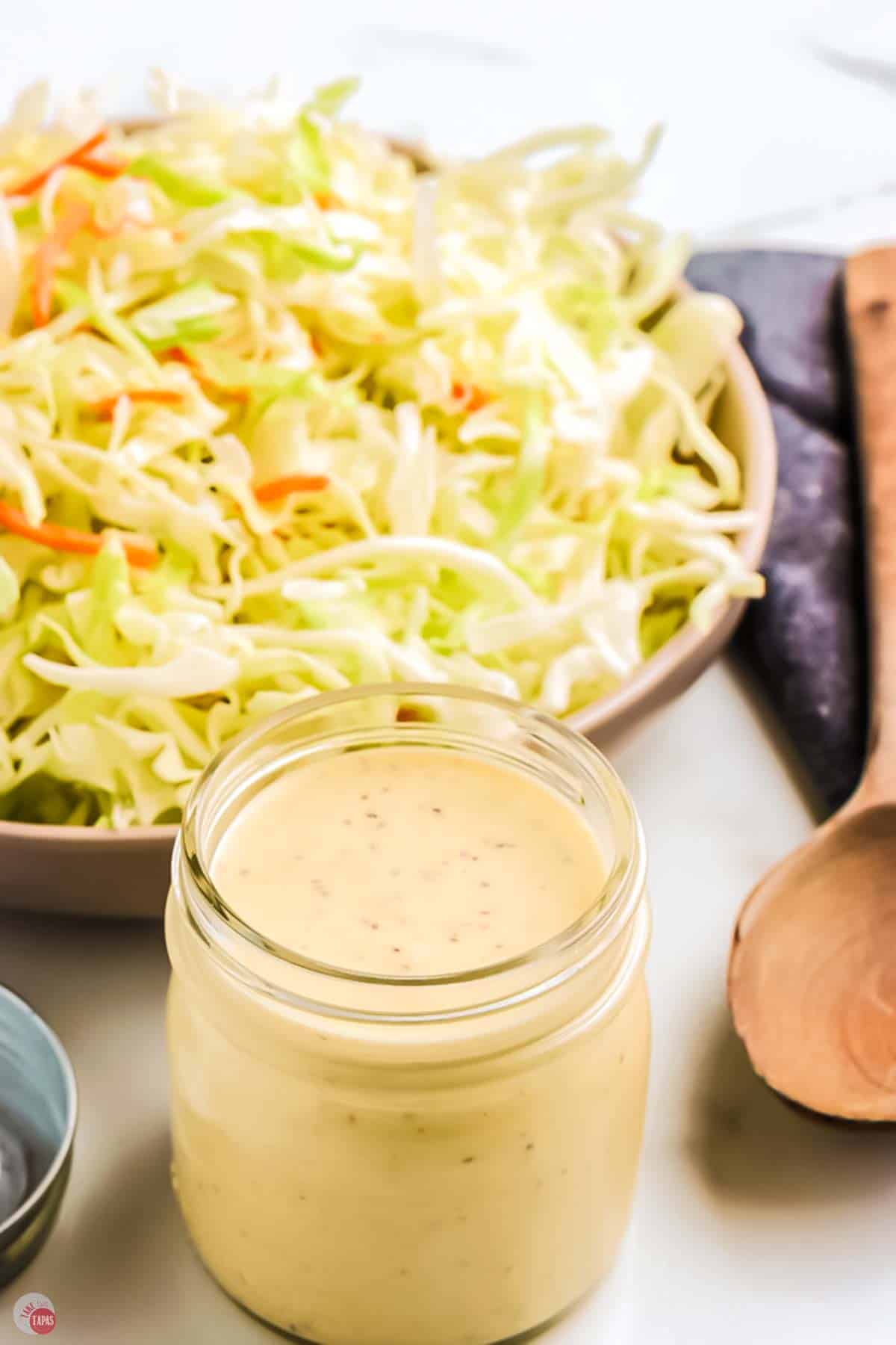 jar of coleslaw dressing next to bowl of shredded cabbage