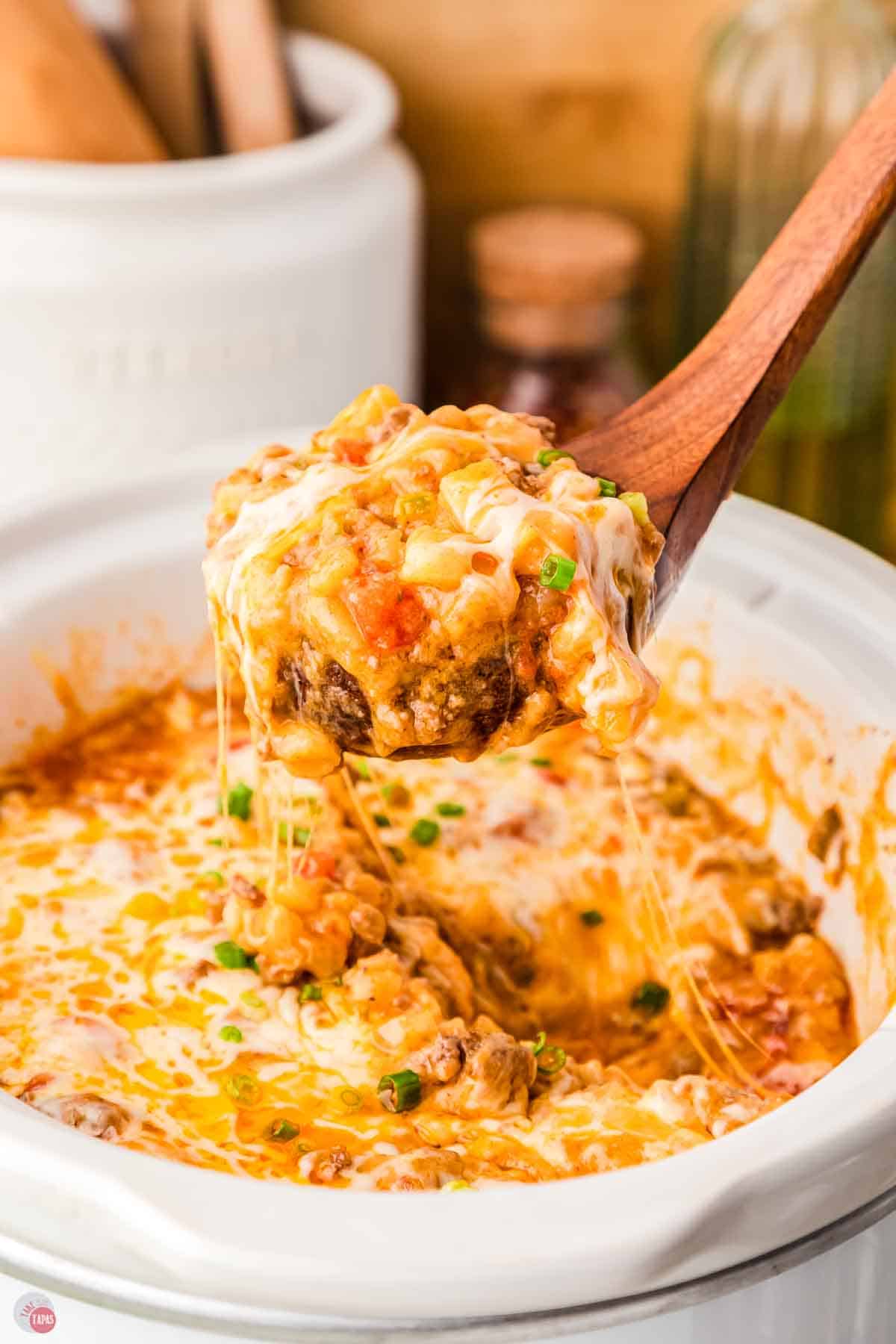 wood spoon scooping casserole out of a white slow cooker pot