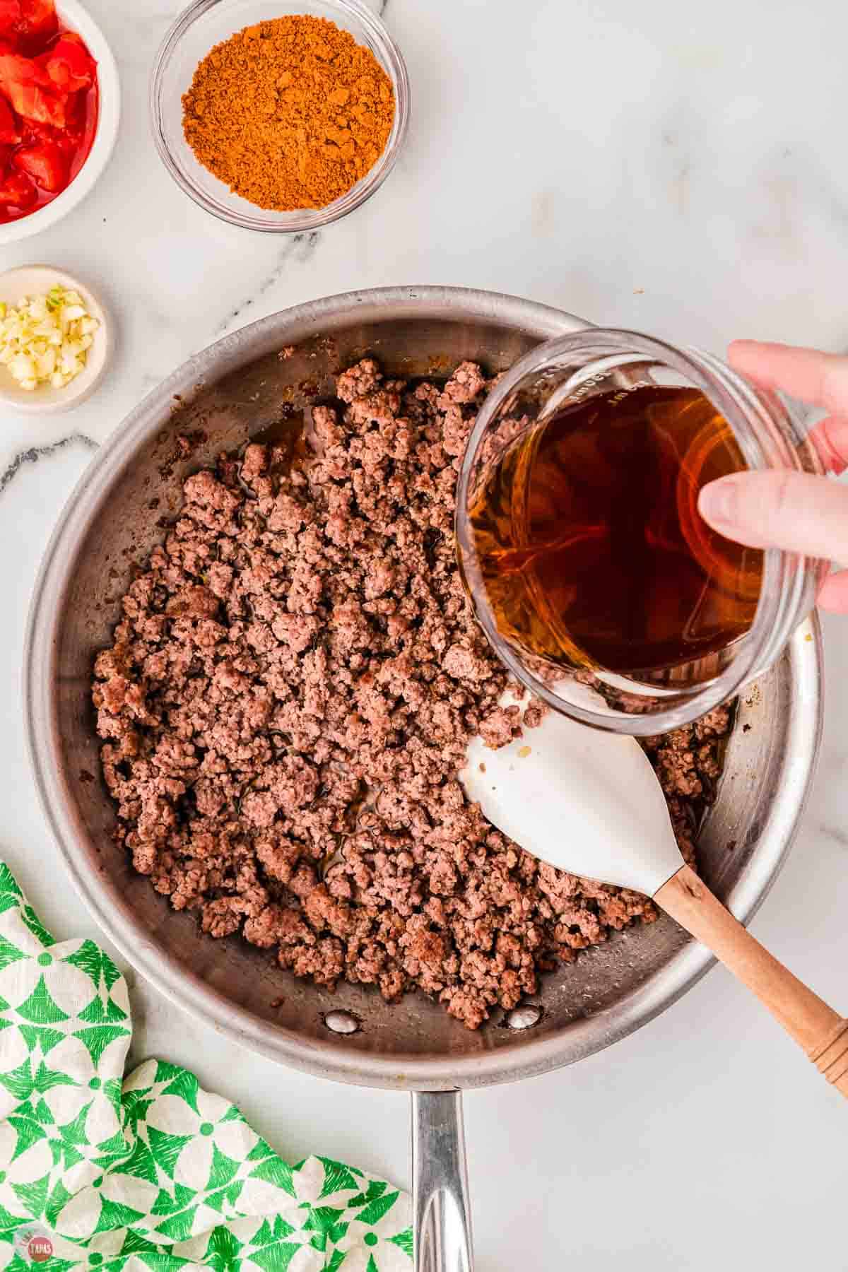 skillet with cooked ground beef and a clear bowl pouring broth into it