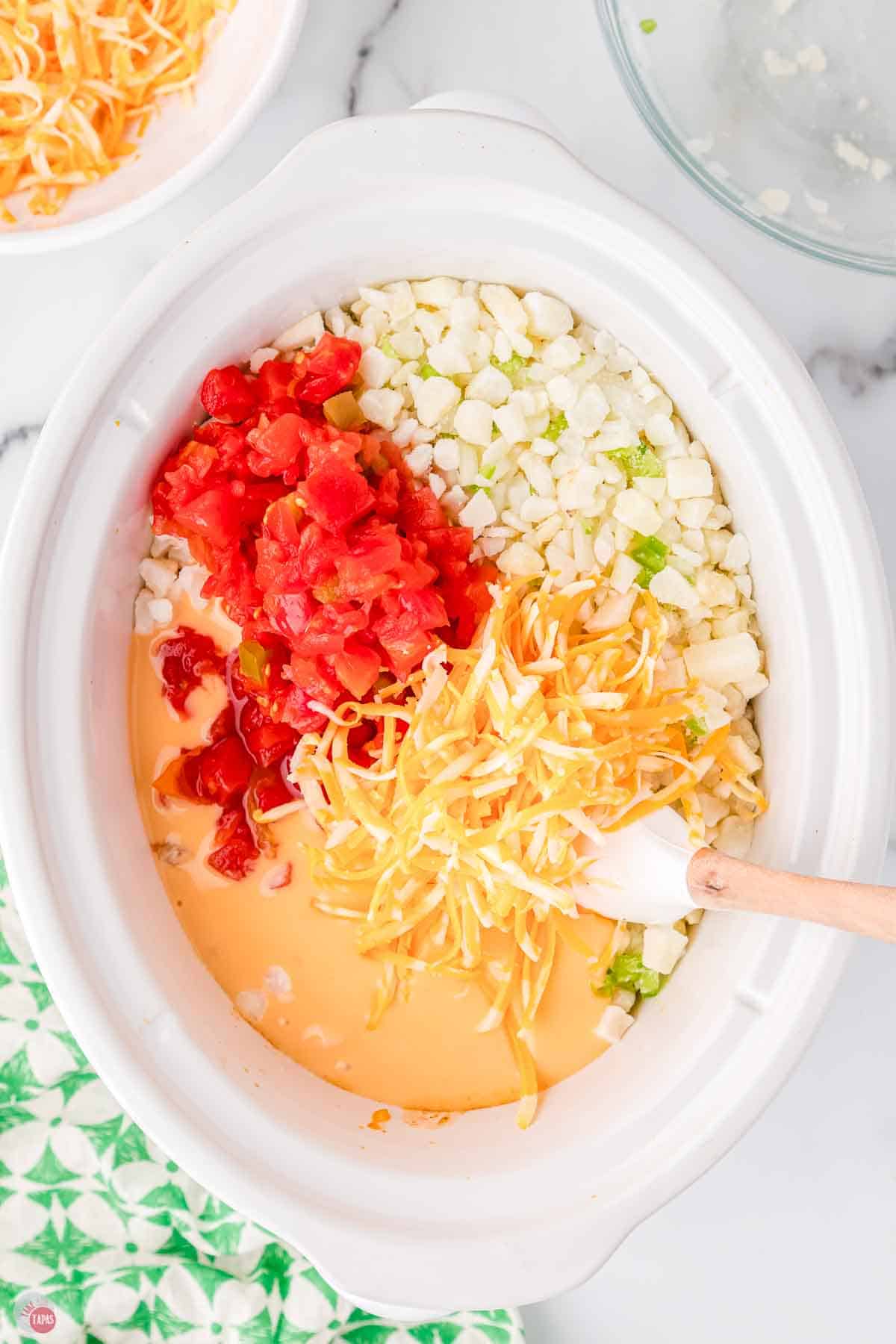white slow cooker bowl with frozen potatoes, Rotel, and shredded cheese in it