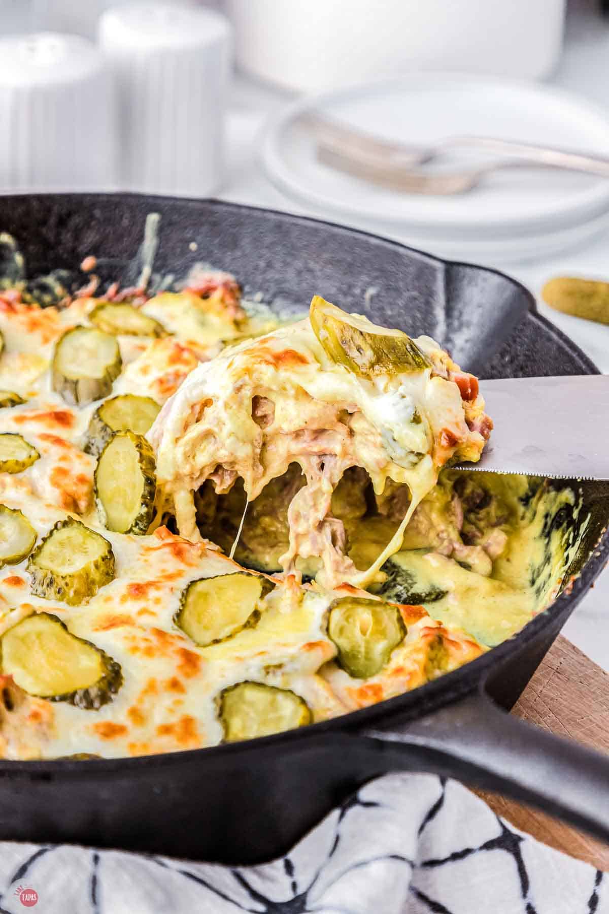 cast iron skillet with a cheesy casserole topped with pickles