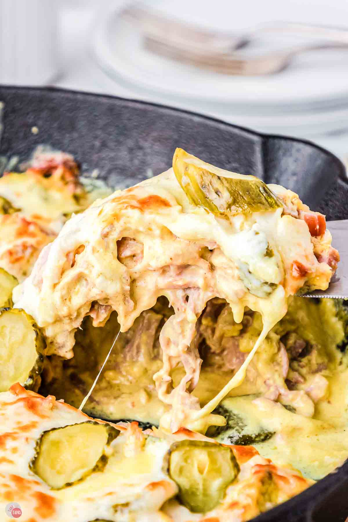 close up of slice of Cuban casserole topped with pickles and cheese