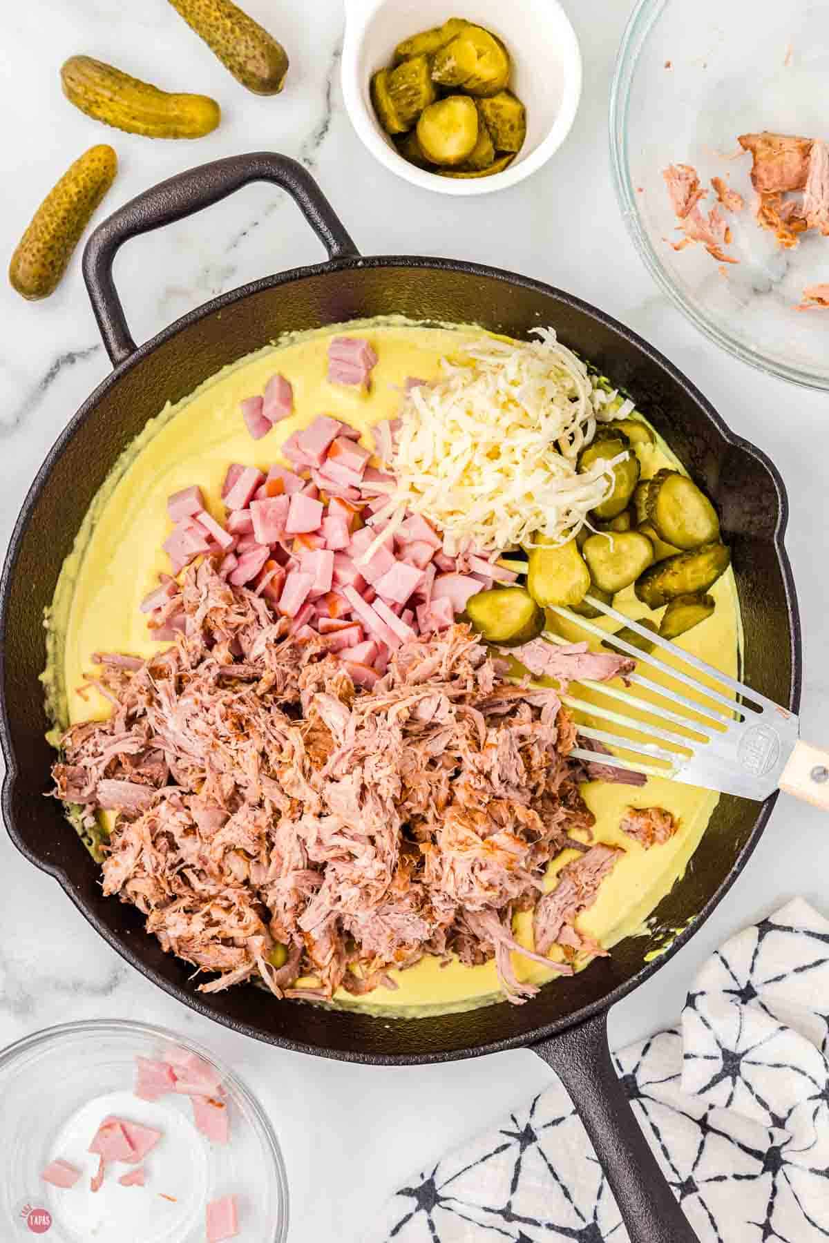 black skillet with mustard sauce, shredded pork, and pickles in it