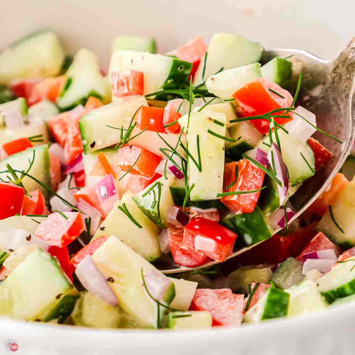 spoon scooping cucumbers and tomatoes out of a bowl