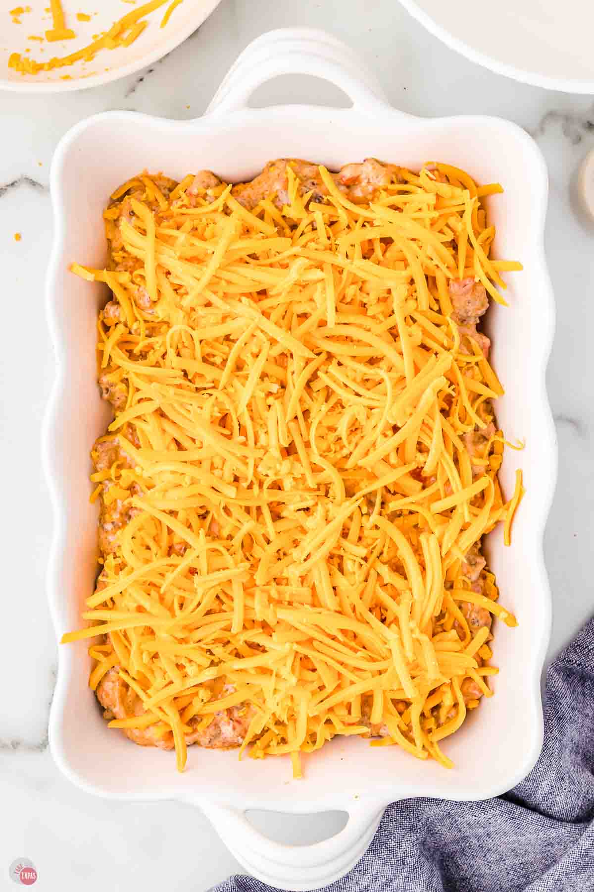 unbaked casserole topped with shredded cheese in a white dish