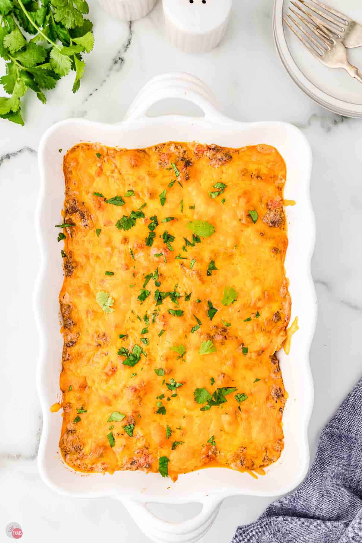 baked cheesy casserole in a white dish topped with chopped parsley