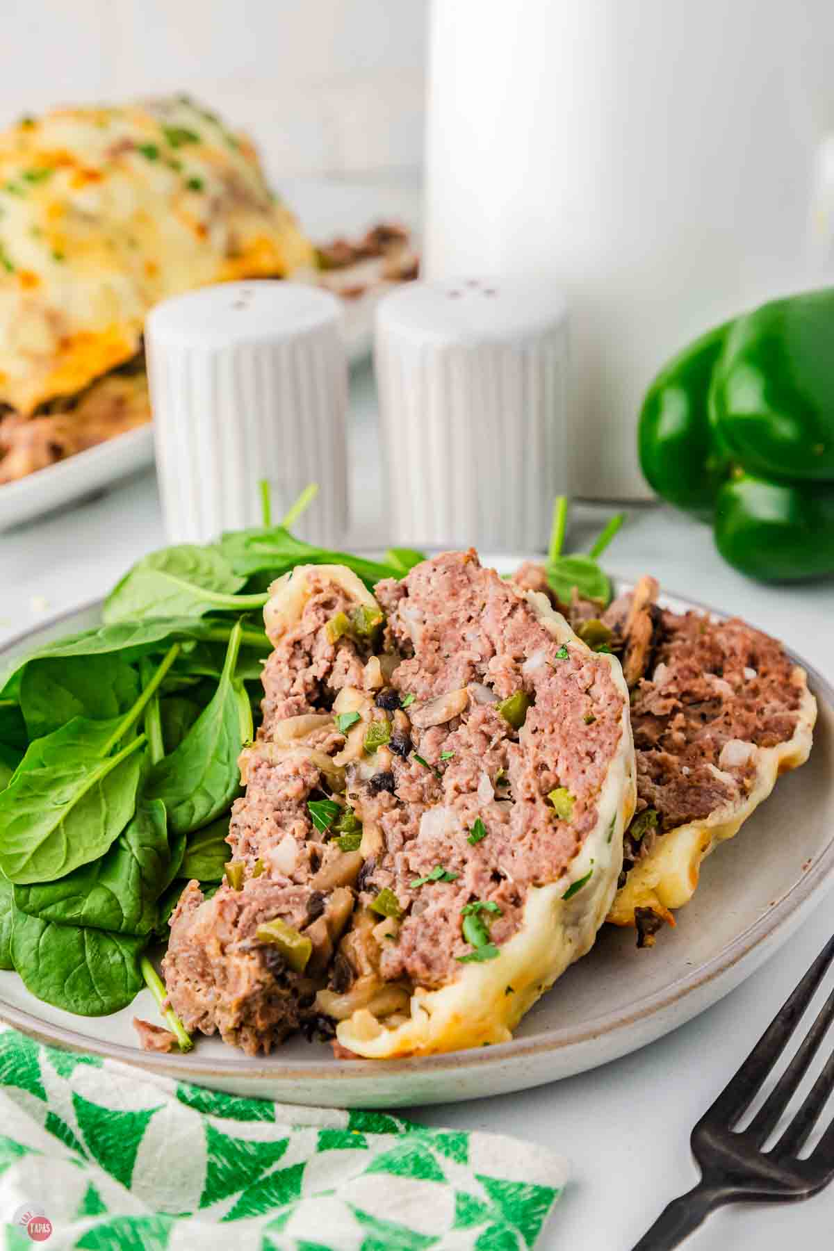 two pieces of meat on a plate next to some fresh spinach