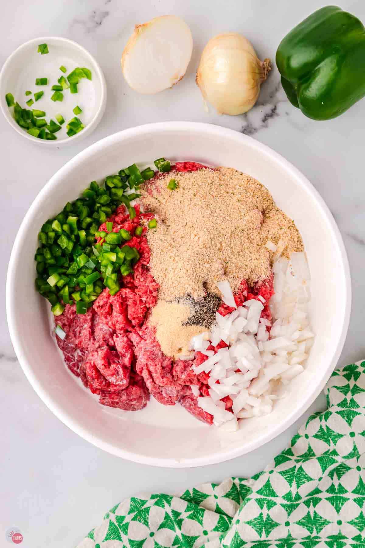 ground beef, peppers, onions, and spices in a white mixing bowl