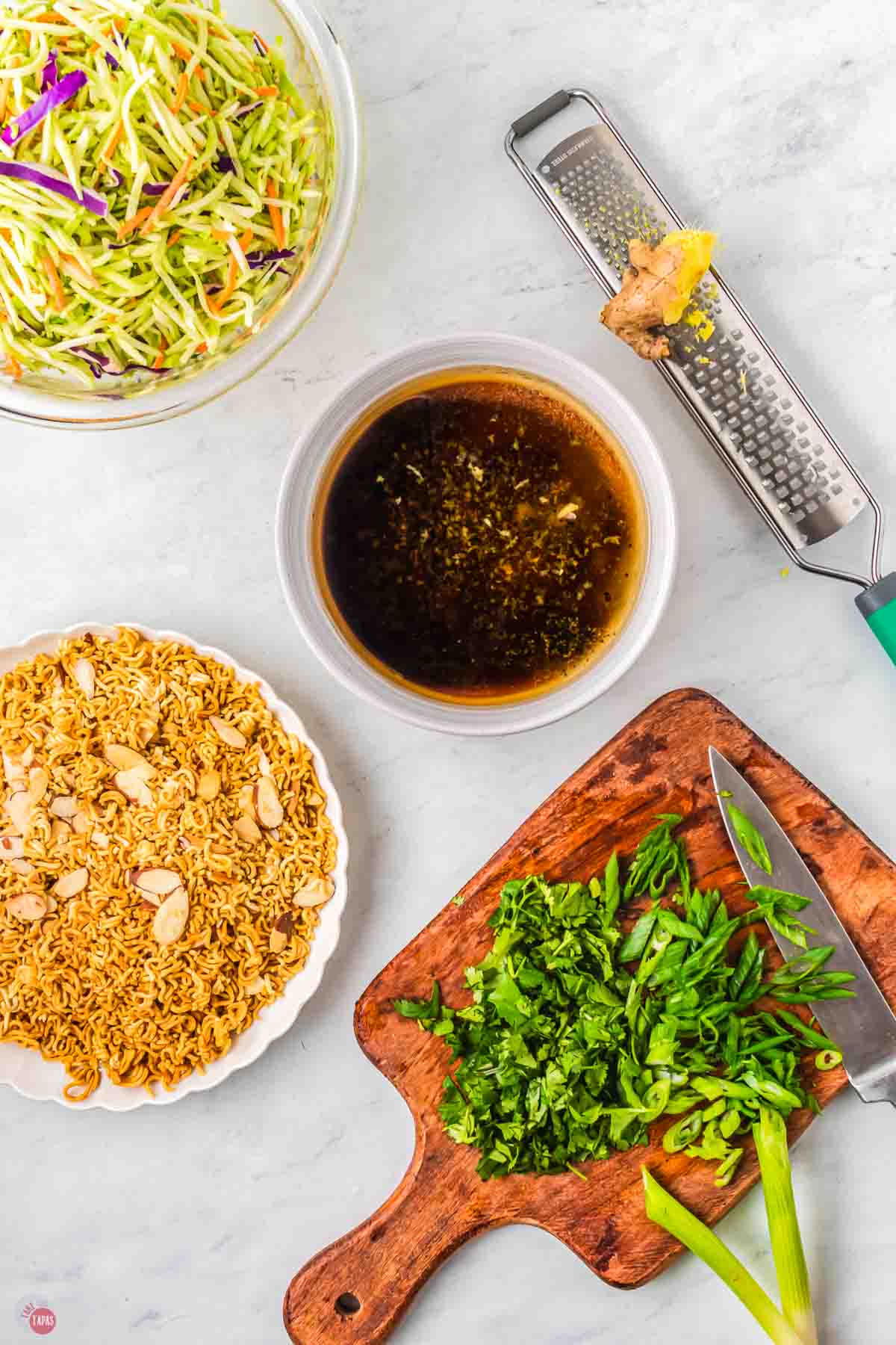 bowl of salad dressing next to a plate of toasted noodles and almonds
