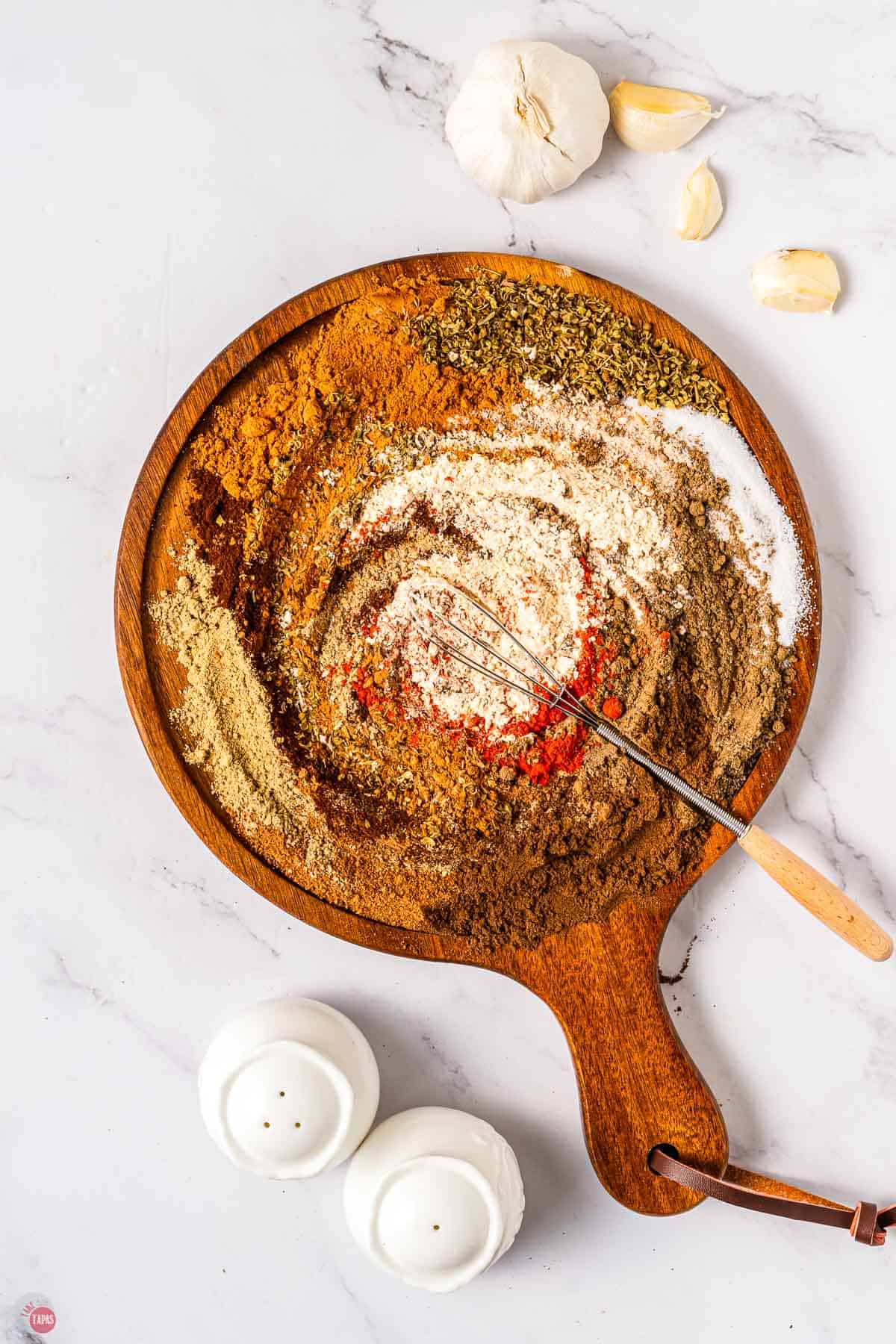 wood board topped with spices and a whisk stirring them together